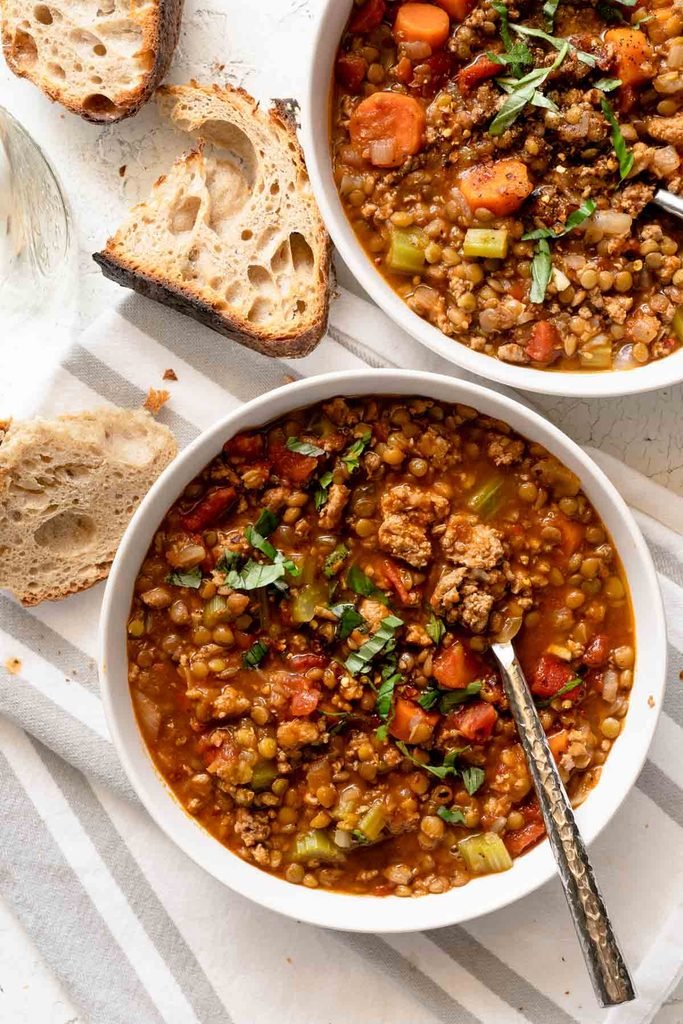 two bowls of thick lentil turkey soup served with crusty artisan bread