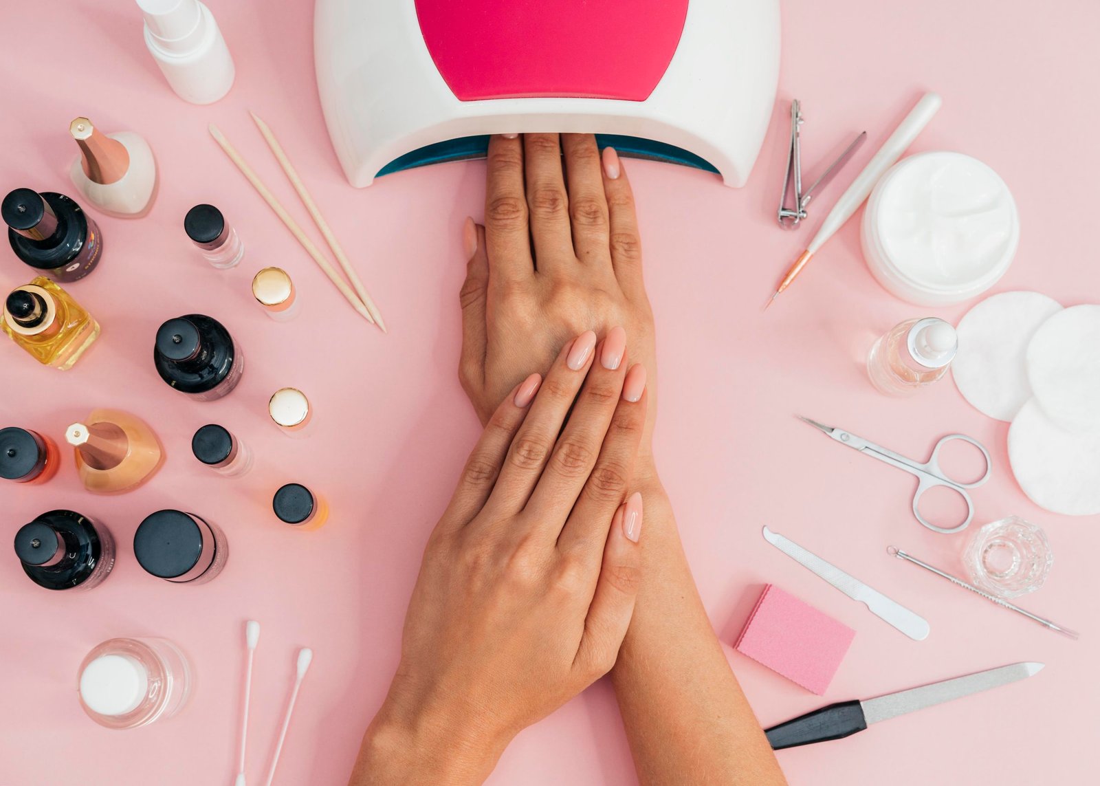 woman receiving a professional manicure with a uv lamp and nail care accessories on pink background