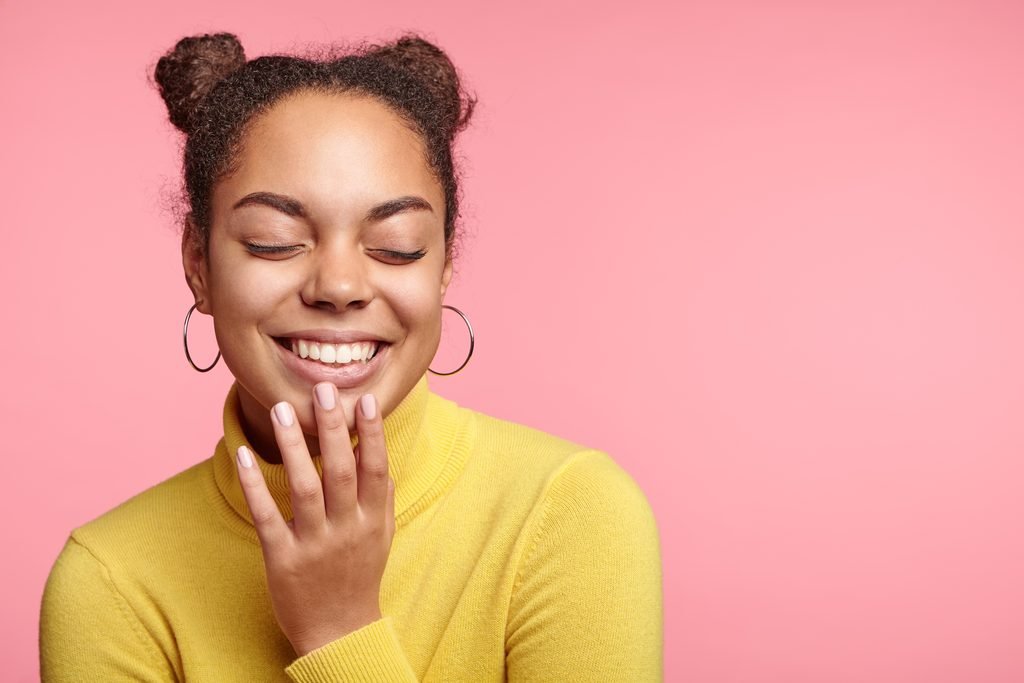 smiling young woman with space buns and yellow turtleneck showing her manicured fingernails
