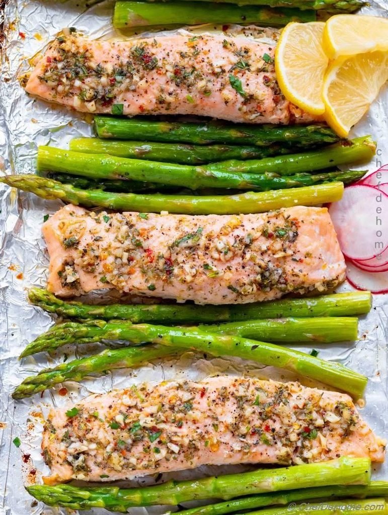 baked salmon fillets and green asparagus spears on a foil-lined baking sheet
