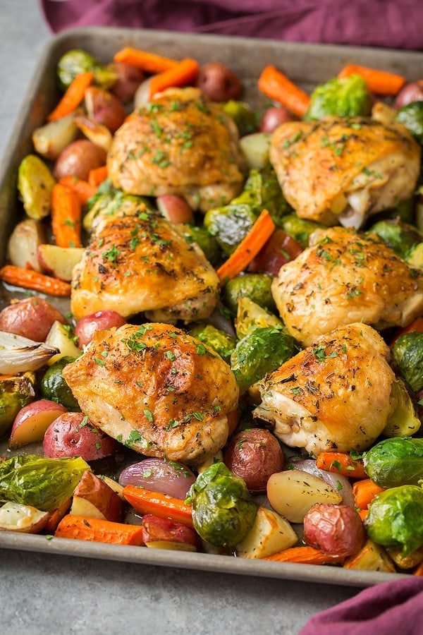 roasted chicken thighs with brussels sprouts, carrots, and potatoes on a baking sheet