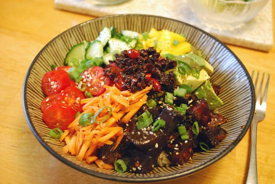 tuna poke bowl filled with diced fish, tomatoes, carrots, avocado, cucumbers, and green onions