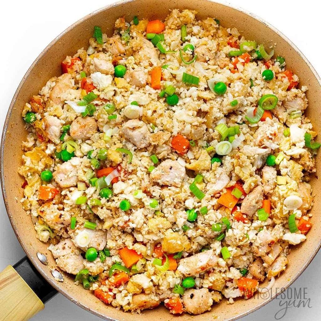 cauliflower chicken fried rice with peas carrots and sliced green onions cooked in a skillet