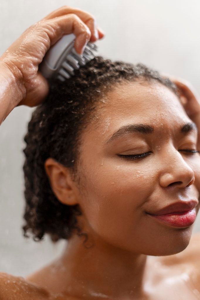 woman smiling with eyes closed while using a scalp massager tool in the shower