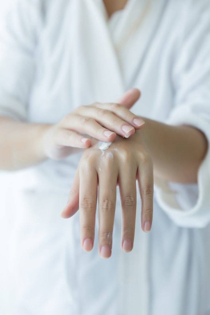 close up of woman applying white moisturizing cream to her hand