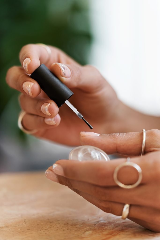 close up of woman applying clear nail polish to her fingernail