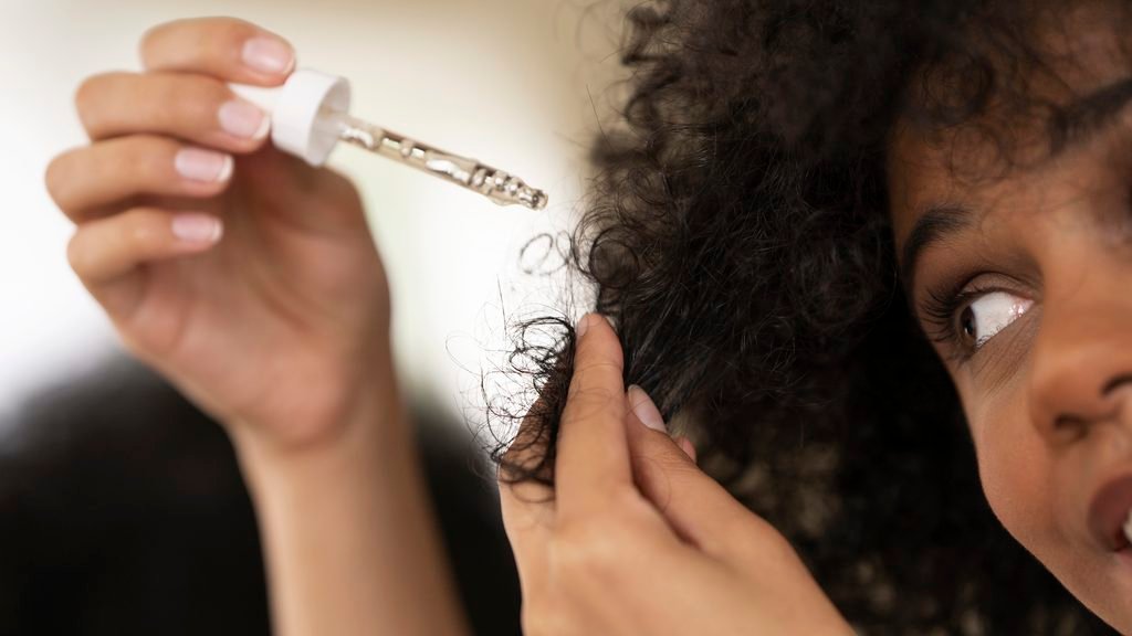 close up of a woman applying hair oil to her curls using a dropper