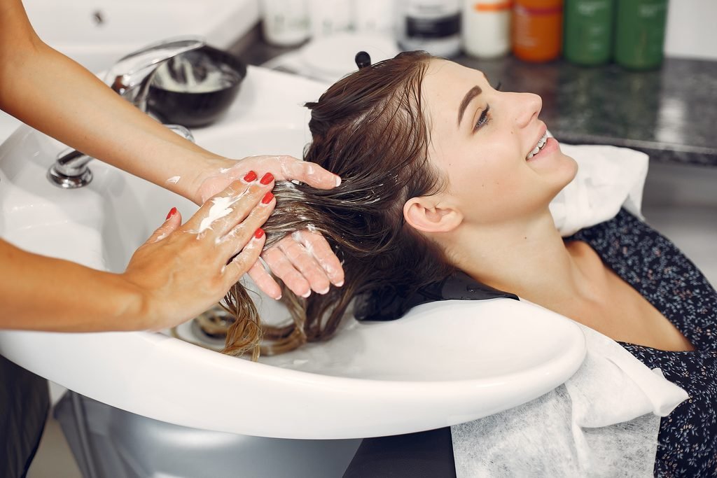 smiling young woman getting her hair washed with product at a hair salon sink
