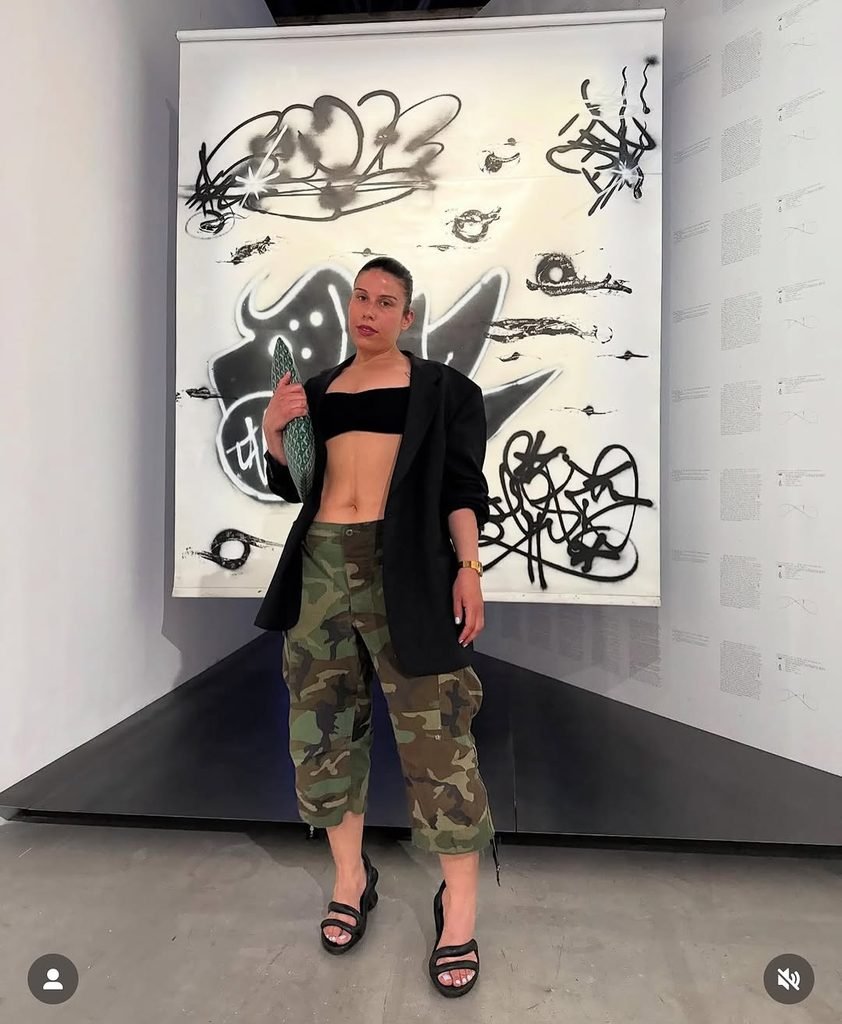 woman wearing a black blazer and camouflage cargo shorts in front of artwork