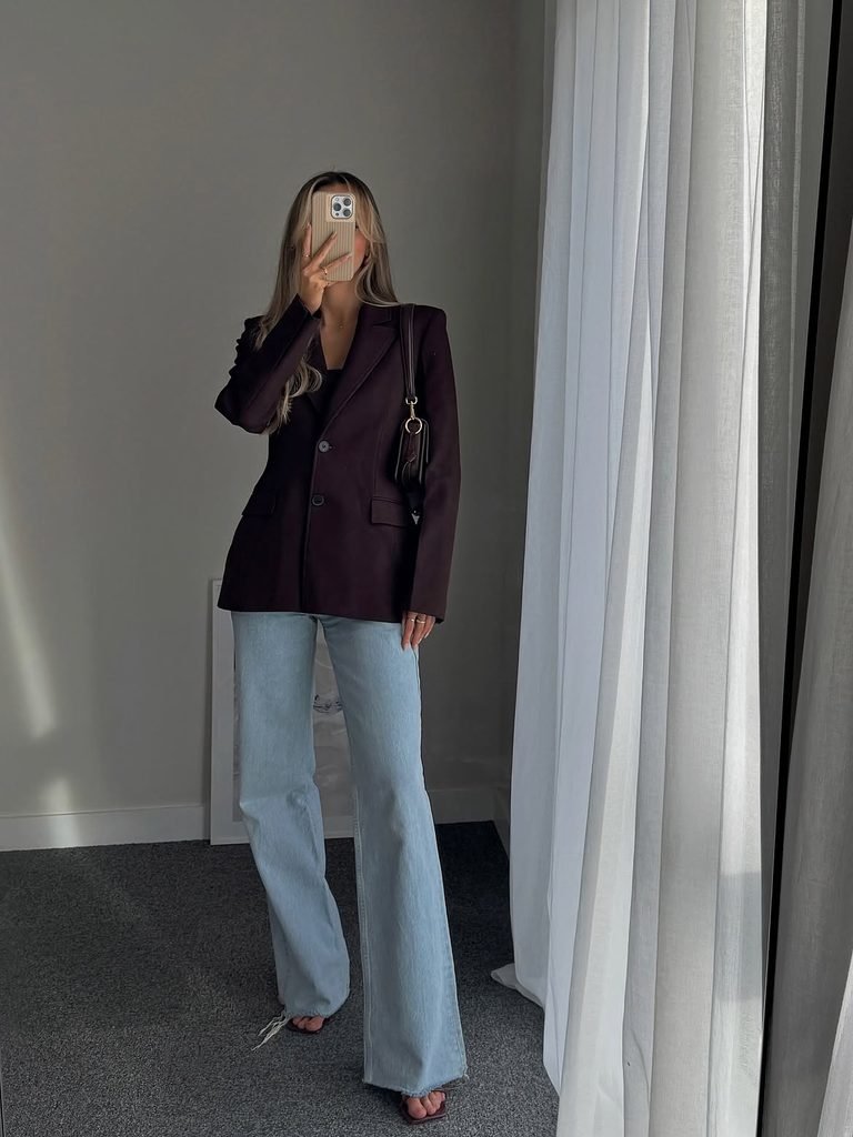woman taking mirror selfie wearing a dark brown blazer and light blue jeans
