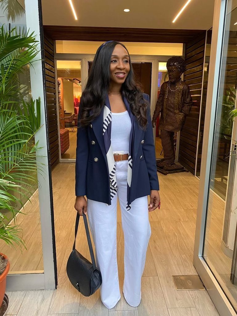 woman in navy double-breasted blazer and white trousers standing in a doorway