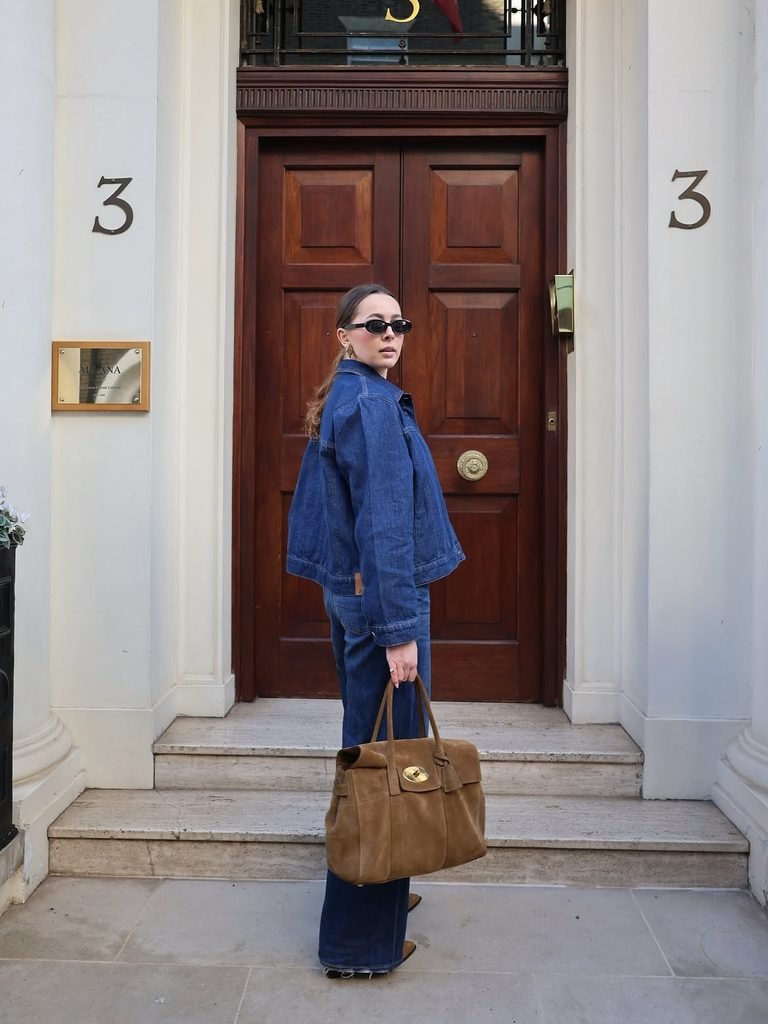 woman in denim jacket and jeans holding a brown suede bag outside