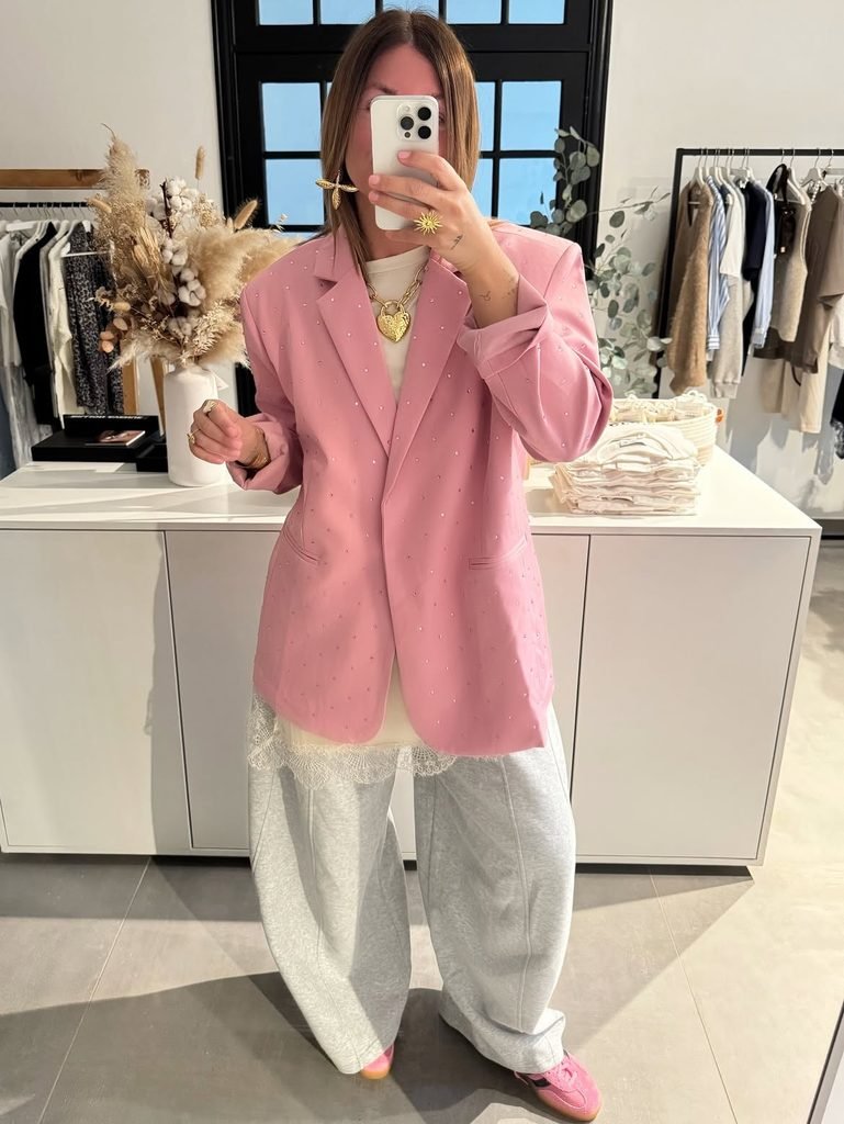 person taking mirror selfie wearing a pink embellished blazer and grey sweatpants