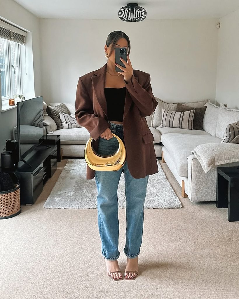 woman in brown oversized blazer and jeans holding a metallic gold handbag