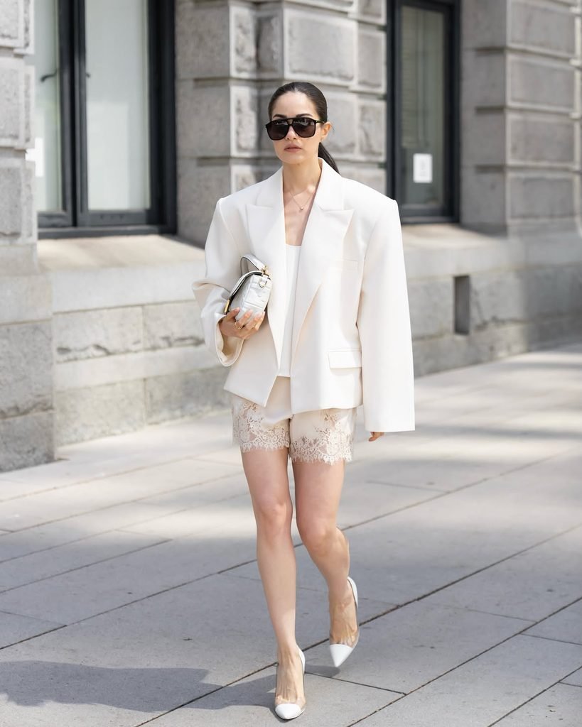 woman walking outside in an oversized white blazer and lace shorts