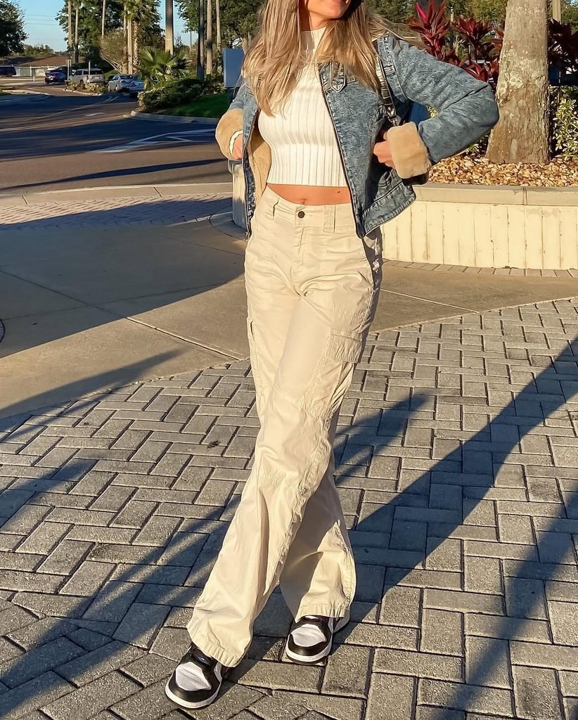 woman wearing cropped white top, denim jacket, and beige cargo pants outdoors