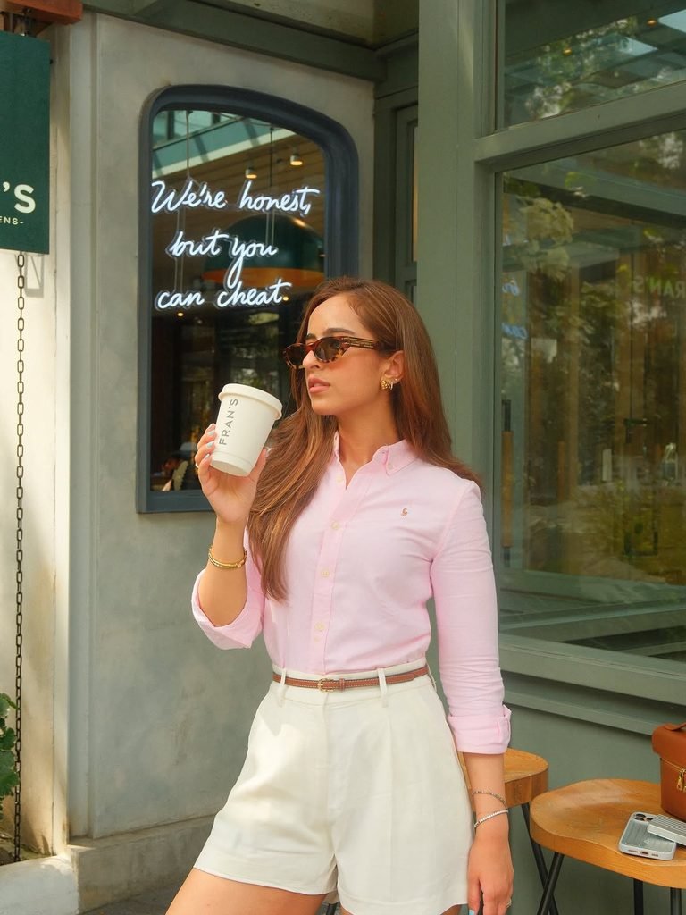 woman in a pink button down shirt holding coffee outside a modern cafe
