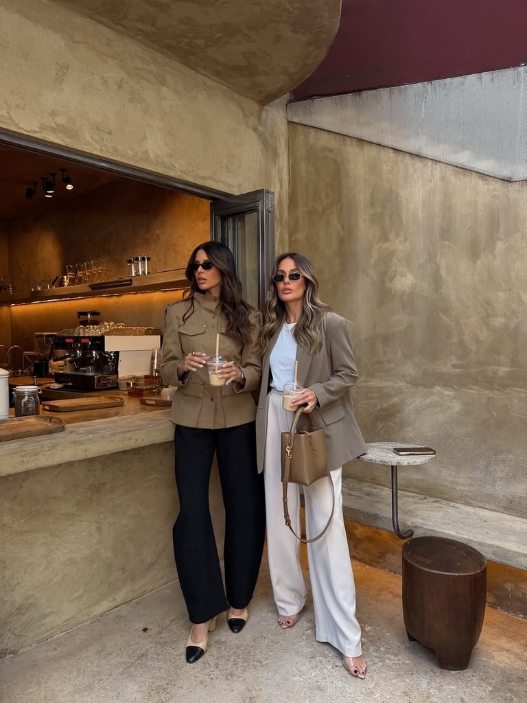 two stylish women holding iced drinks standing in front of a modern coffee shop