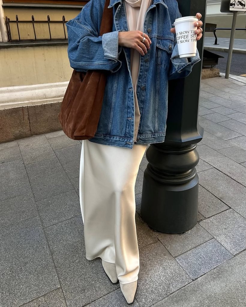 woman in oversized denim jacket, cream satin maxi skirt, and beige boots