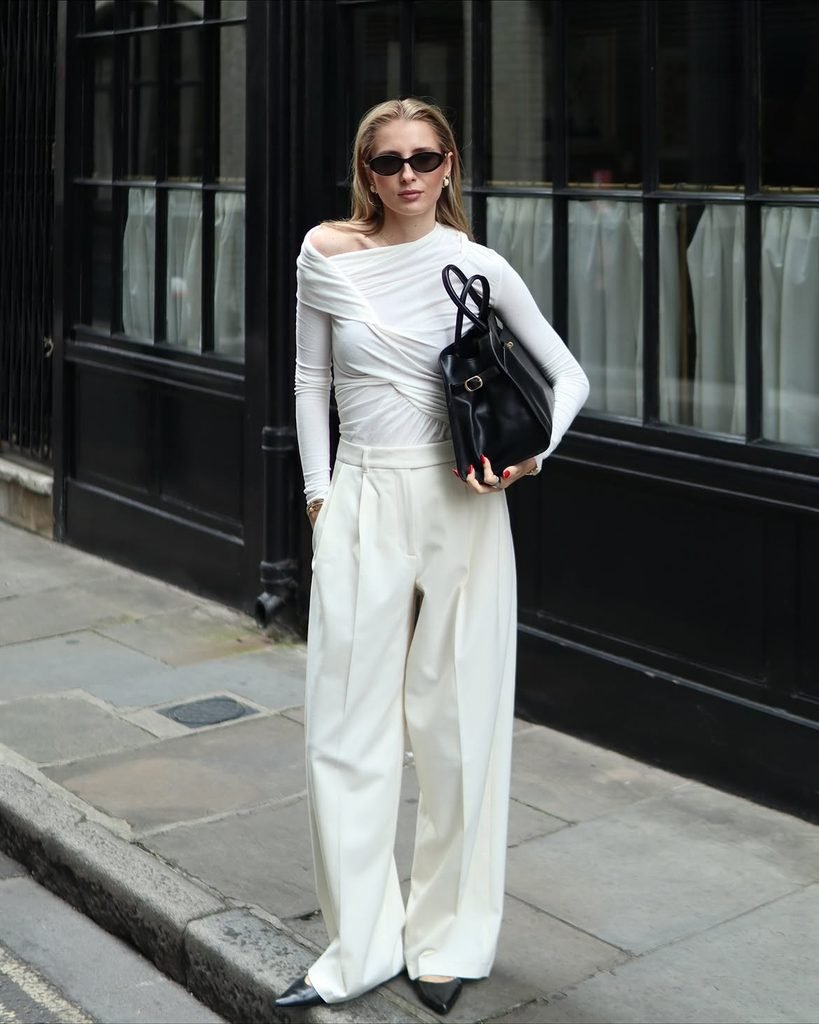 woman in black asymmetrical top and white trousers standing outdoors