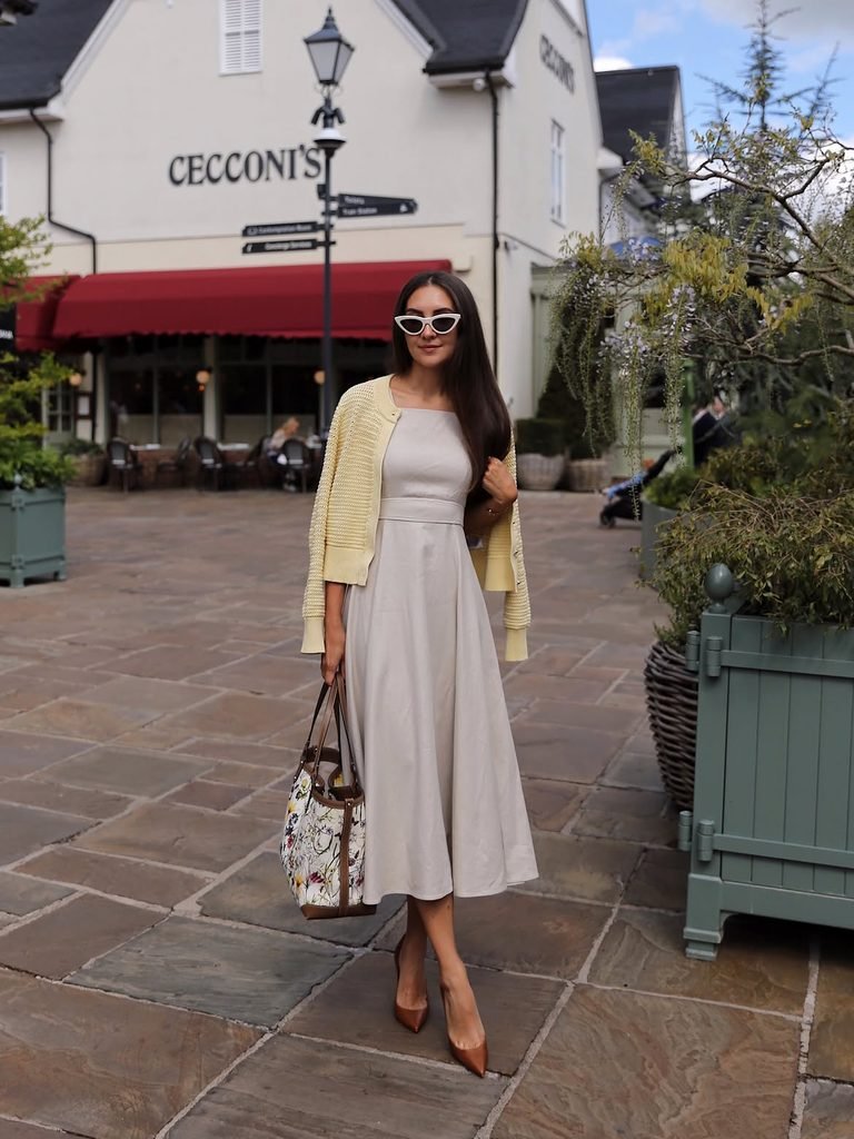 woman wearing a beige midi dress and yellow cardigan carrying a floral tote bag