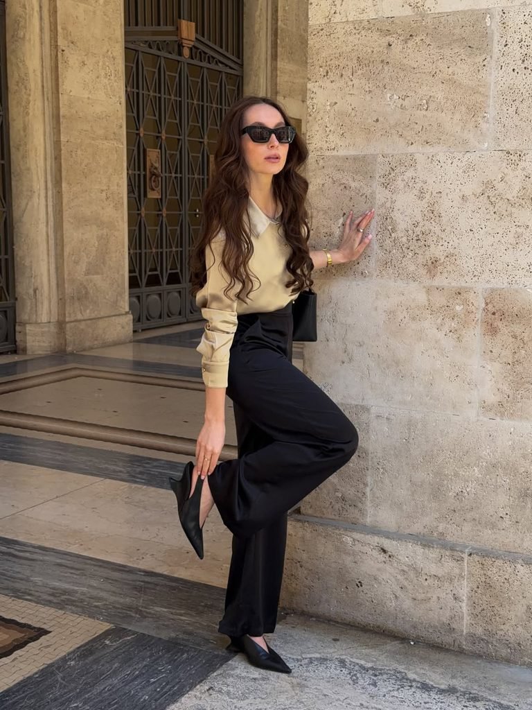 woman wearing a beige satin blouse black wide-leg trousers and pointed heels outdoors