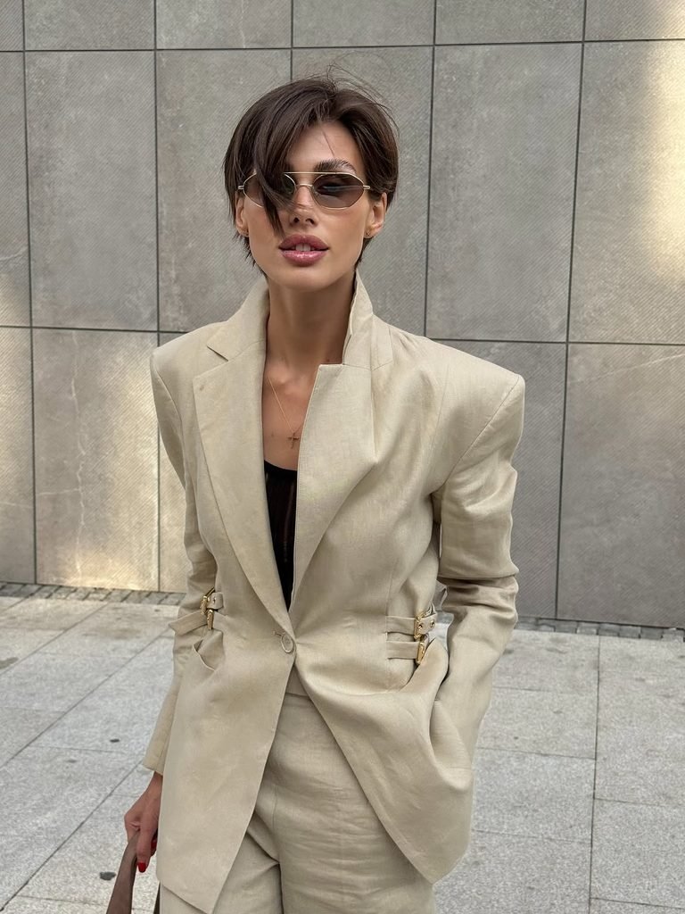 woman with short hair wearing a beige linen blazer suit and sunglasses