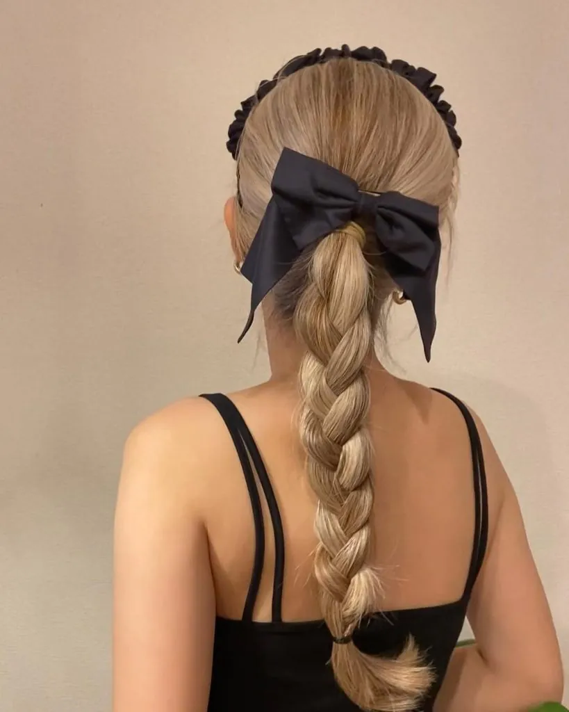 back view of blonde braided ponytail hairstyle accessorized with a large black bow