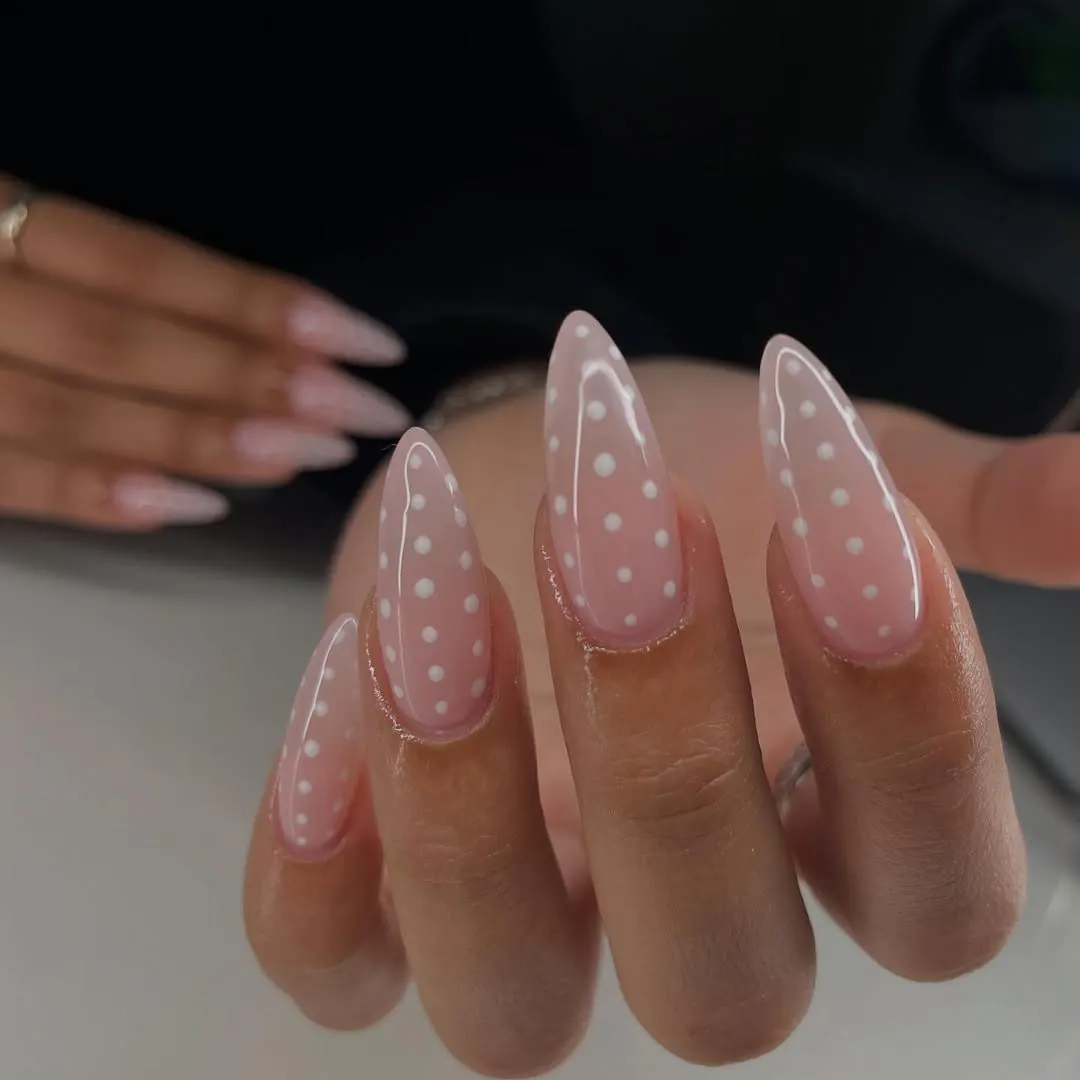 sheer pink stiletto shaped manicure featuring a delicate white polka dot design