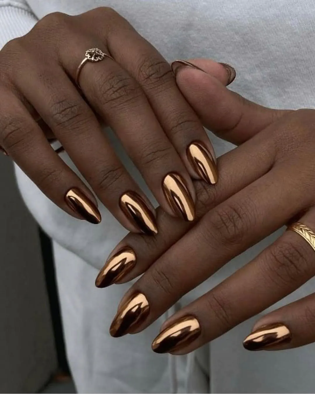metallic bronze chrome manicure on long almond shaped nails with minimalist gold rings