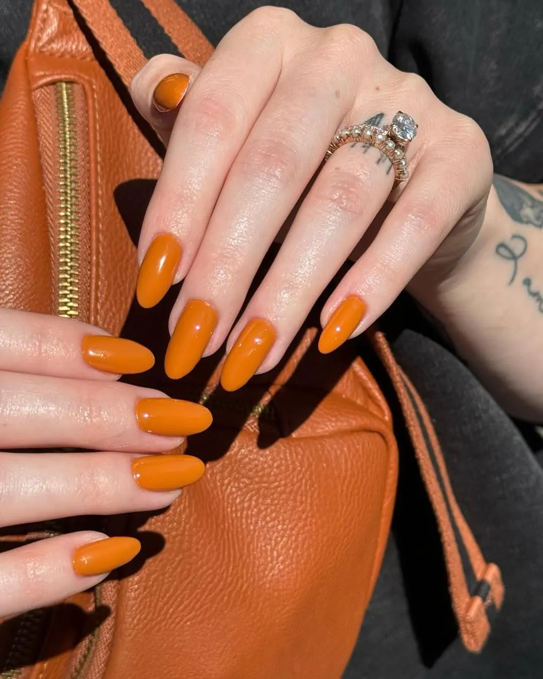 burnt orange oval manicure on a hand resting against a matching leather bag