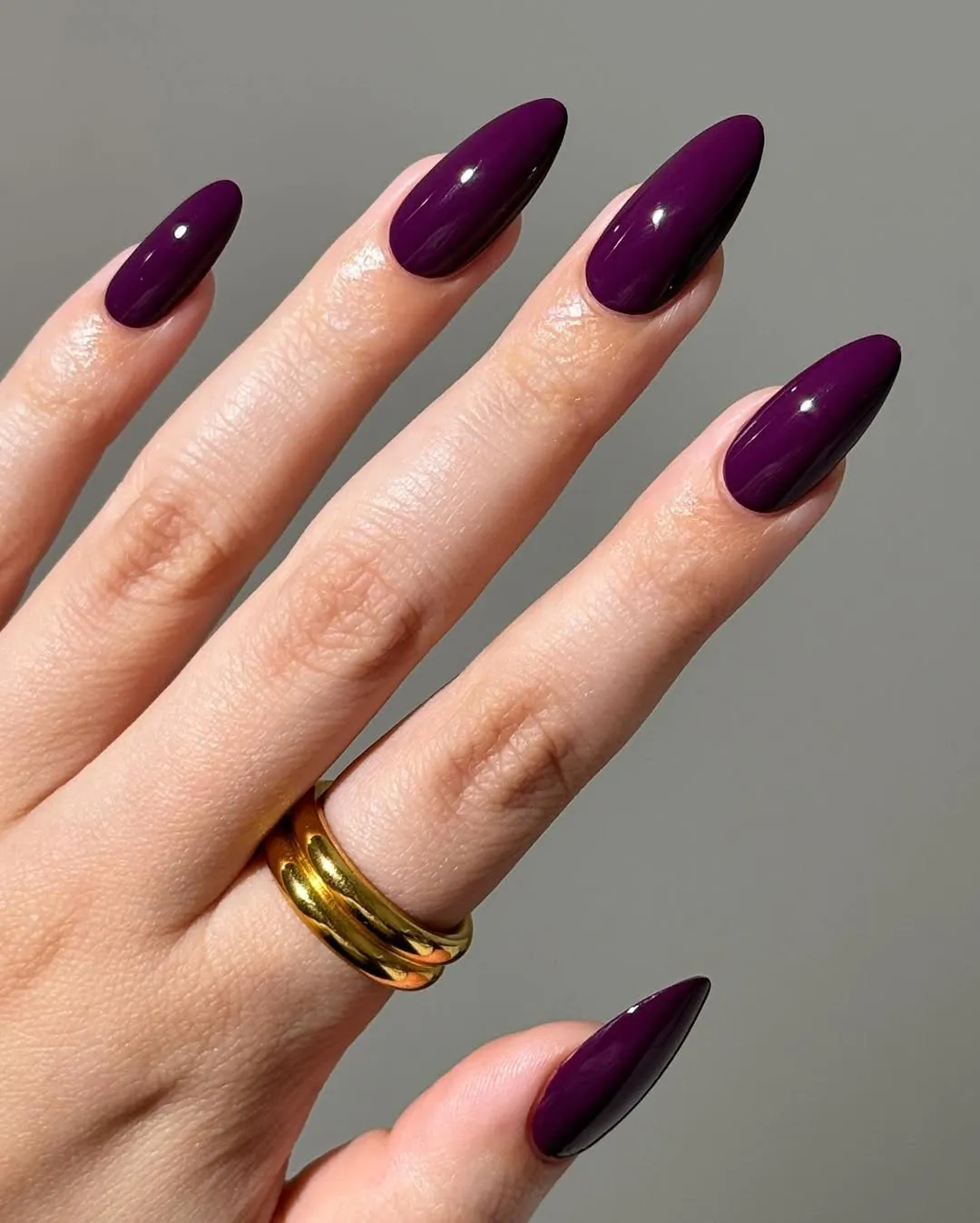 deep plum purple almond shaped manicure on a hand wearing stacked gold rings