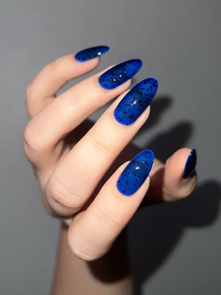 long almond shaped translucent blue nails featuring black speckled glitter accents