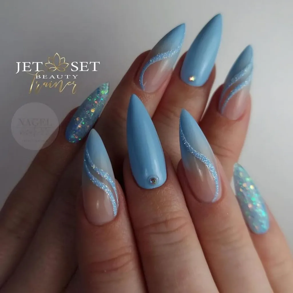 light blue stiletto nails with glittery swirls and rhinestone accents