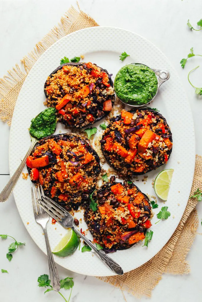 four portobello mushrooms stuffed with vegetable quinoa salad served on a platter with green sauce