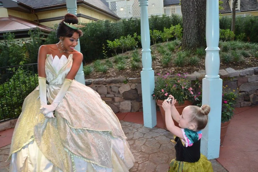 young girl taking a photo of a woman dressed as princess tiana