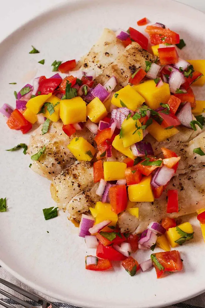 grilled halibut fillet served on a white plate topped with a colorful mango salsa