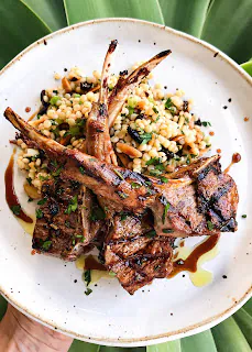 grilled lamb chops served over a bed of couscous salad on a white plate