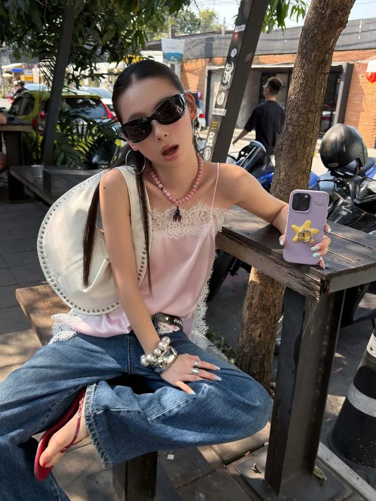 woman wearing a pink satin camisole and wide-leg blue jeans sitting outdoors at a table