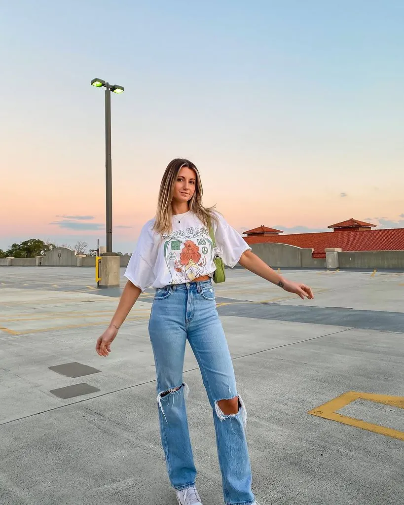 woman wearing a white graphic t-shirt and ripped light wash jeans on a rooftop