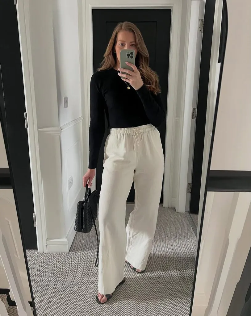 woman in black long sleeve top and cream wide leg linen trousers taking mirror selfie