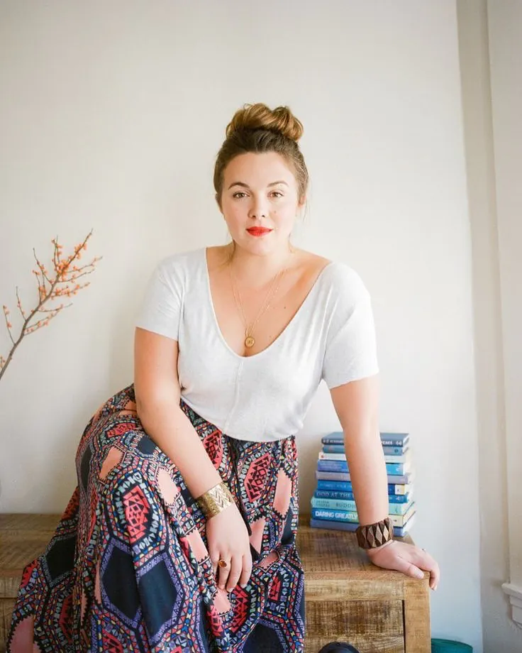 woman with a hair bun wearing a white v-neck shirt and patterned maxi skirt