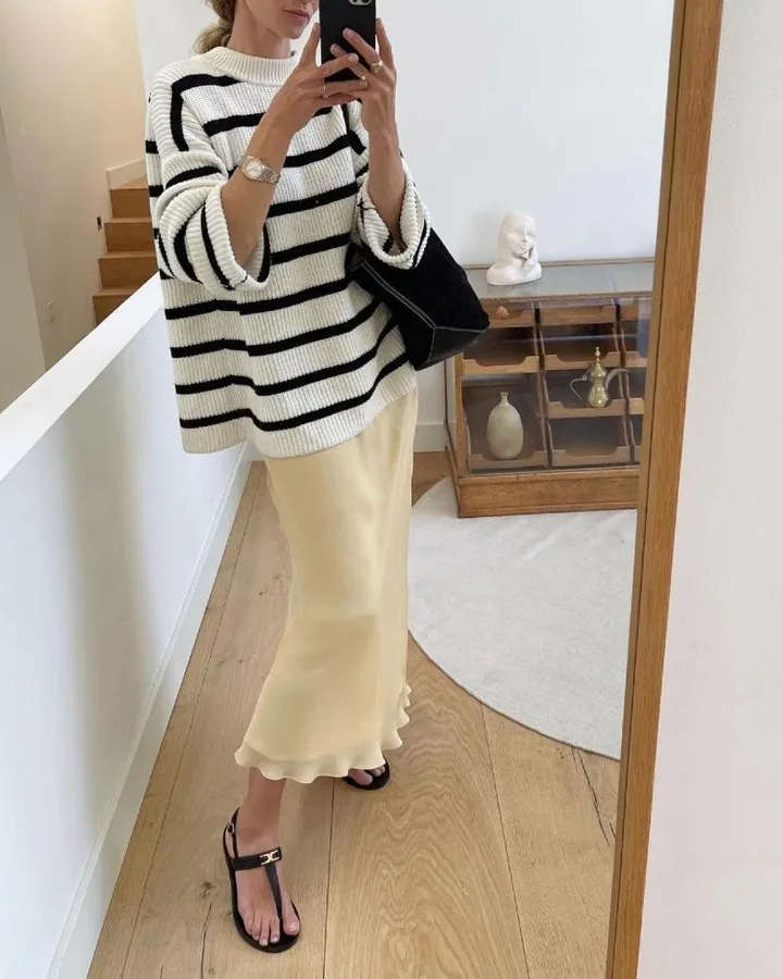 woman in striped knit sweater and cream silk skirt taking mirror selfie