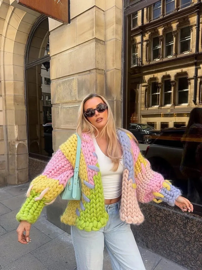 woman on city street wearing chunky multicolored knit cardigan and light wash jeans