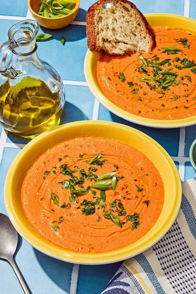 two yellow bowls of chilled gazpacho soup garnished with fresh herbs and olive oil
