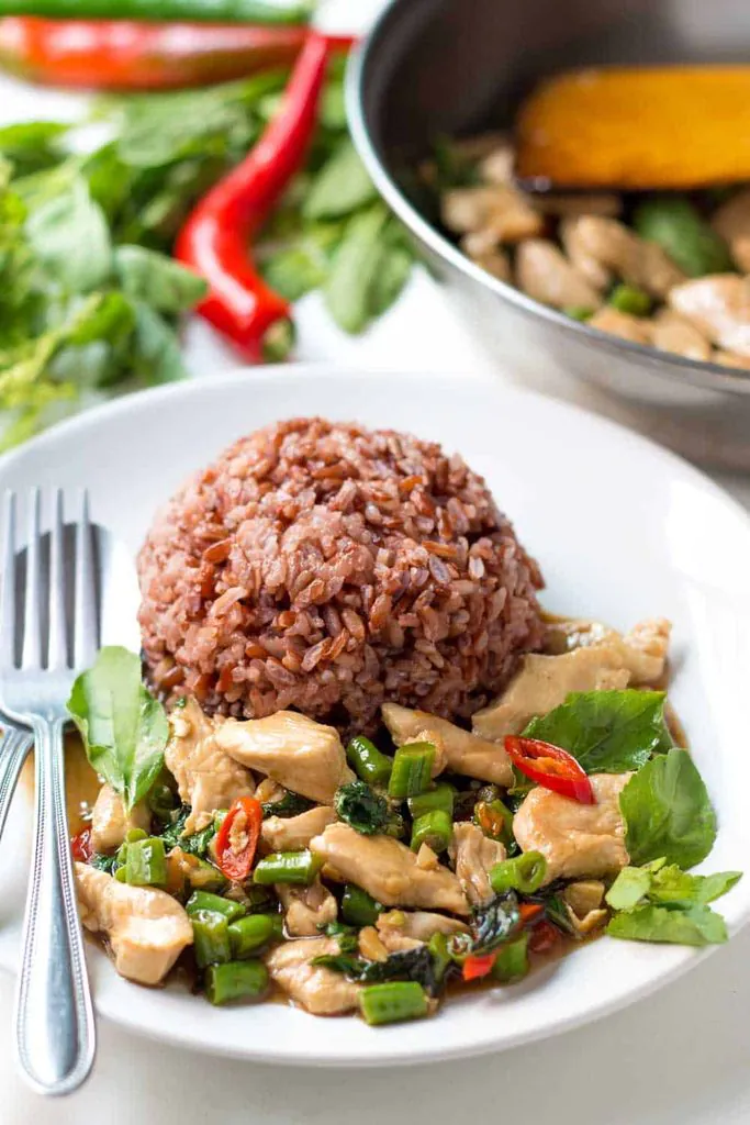thai holy basil chicken stir fry served with red rice on a white plate