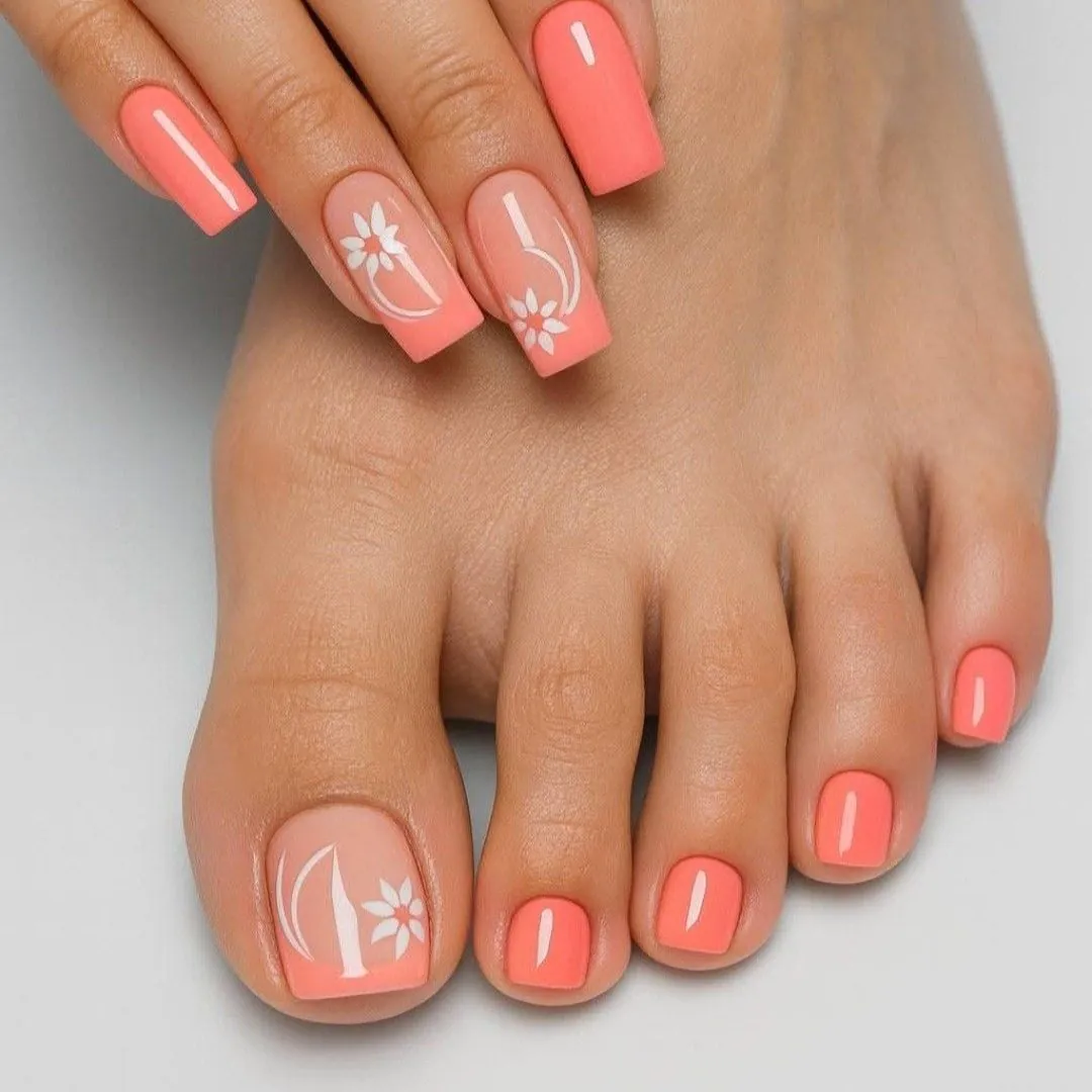 matching coral manicure and pedicure with white floral nail art on the accent nails