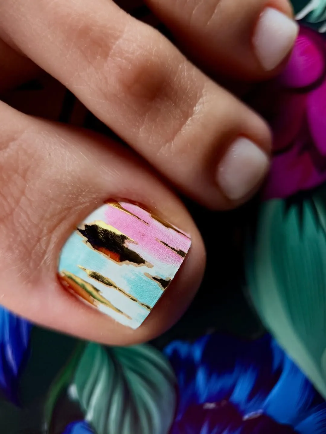 abstract colorful pink and blue nail wrap design with metallic gold streaks on a toenail
