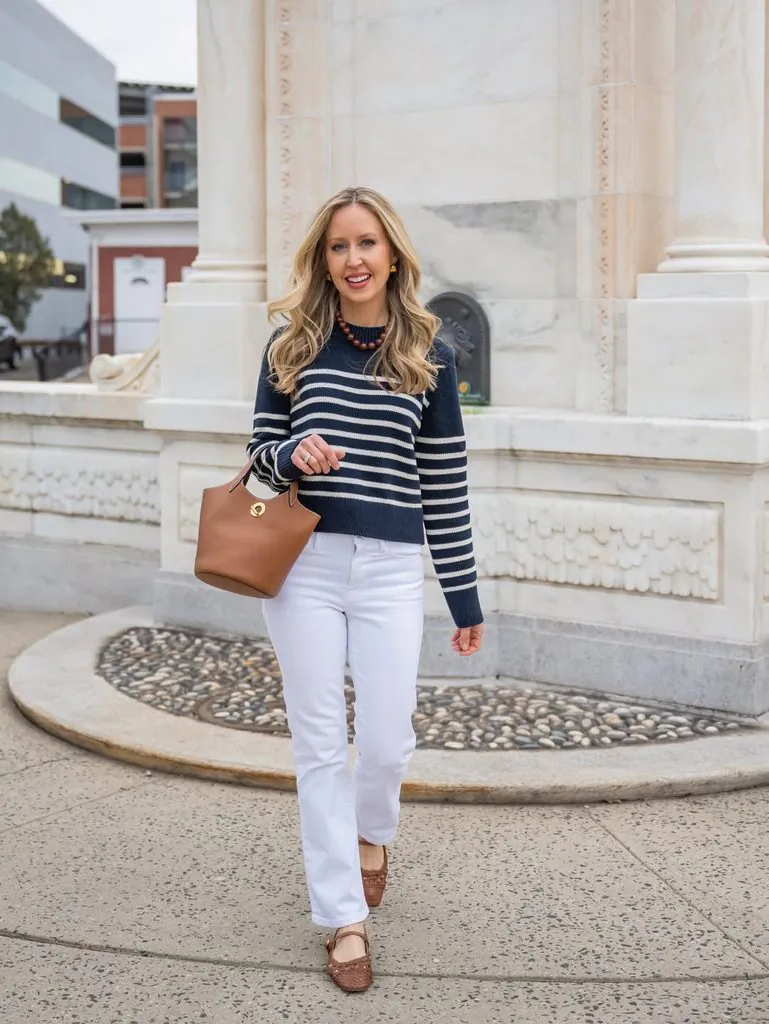 woman in a striped sweater and white jeans walking near a fountain