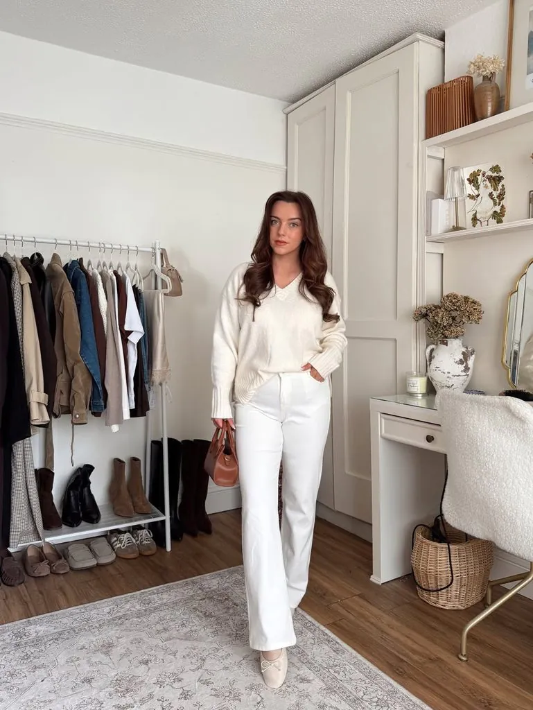 woman wearing a cream v-neck sweater and white jeans holding a purse
